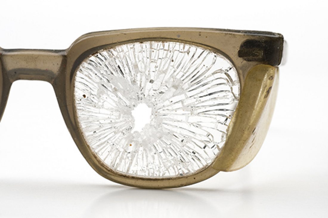 Close up of shattered lens of a pair of safety glasses showing the value of eye protection. Horizontal format with white background.
